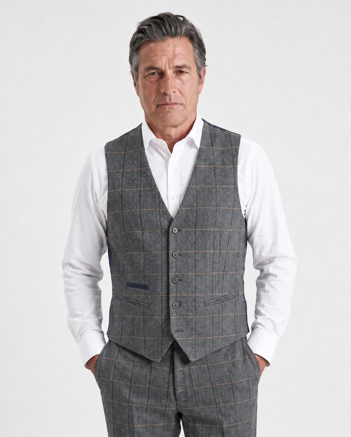 A man wearing a gray windowpane plaid waistcoat vest over a white long-sleeve shirt, paired with matching gray trousers, against a light gray studio background.