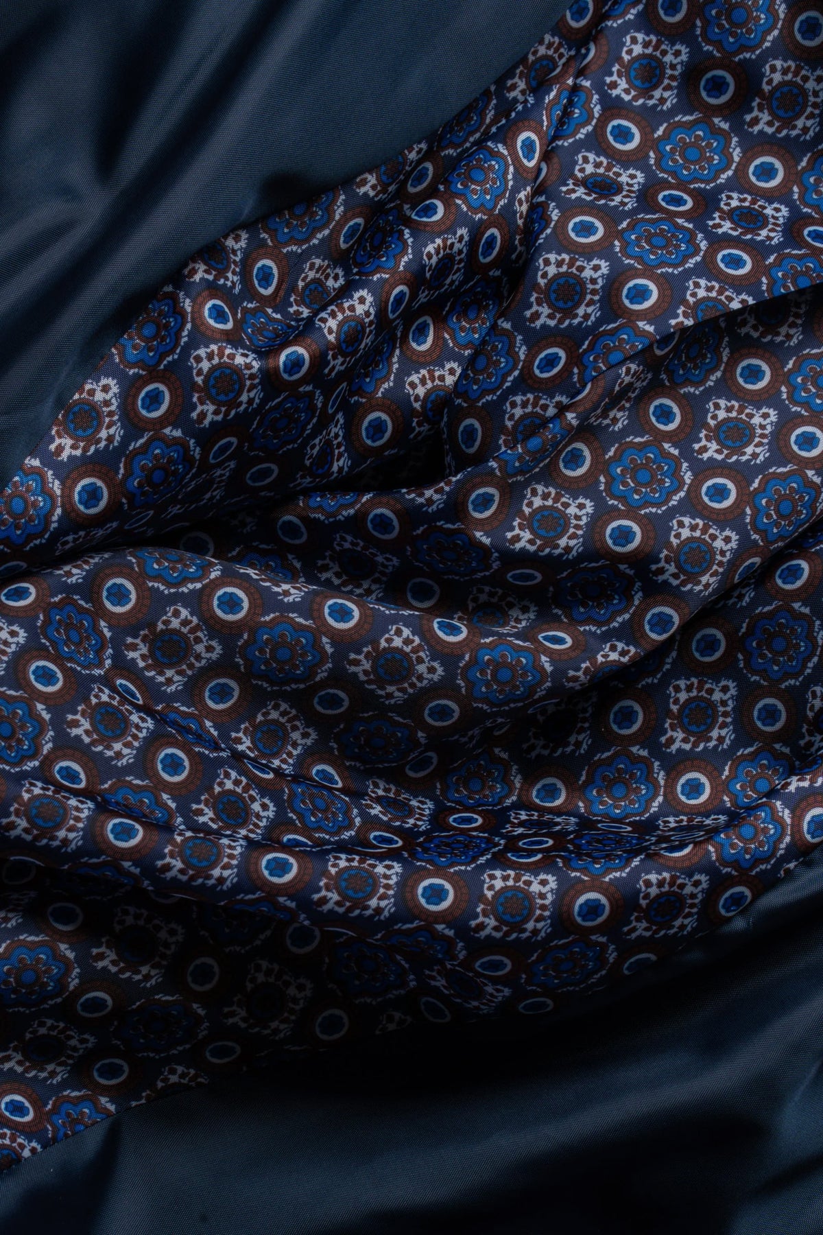 A close-up of draped fabric with a dark navy base and an allover repeating circular medallion pattern in blue, white, and brown.