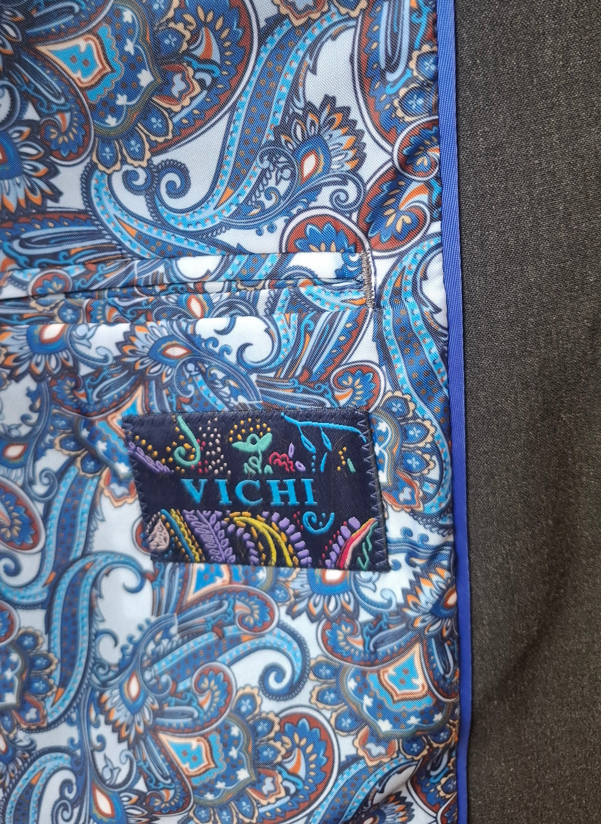 Close-up of a suit pocket with a blue paisley pattern and 'Vichi' branding.