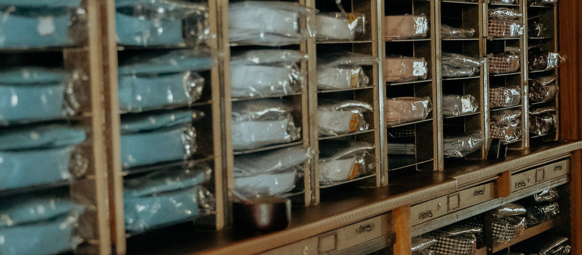 Wooden shelving filled with neatly folded garments in clear plastic packaging, arranged in rows inside a storage or retail space.