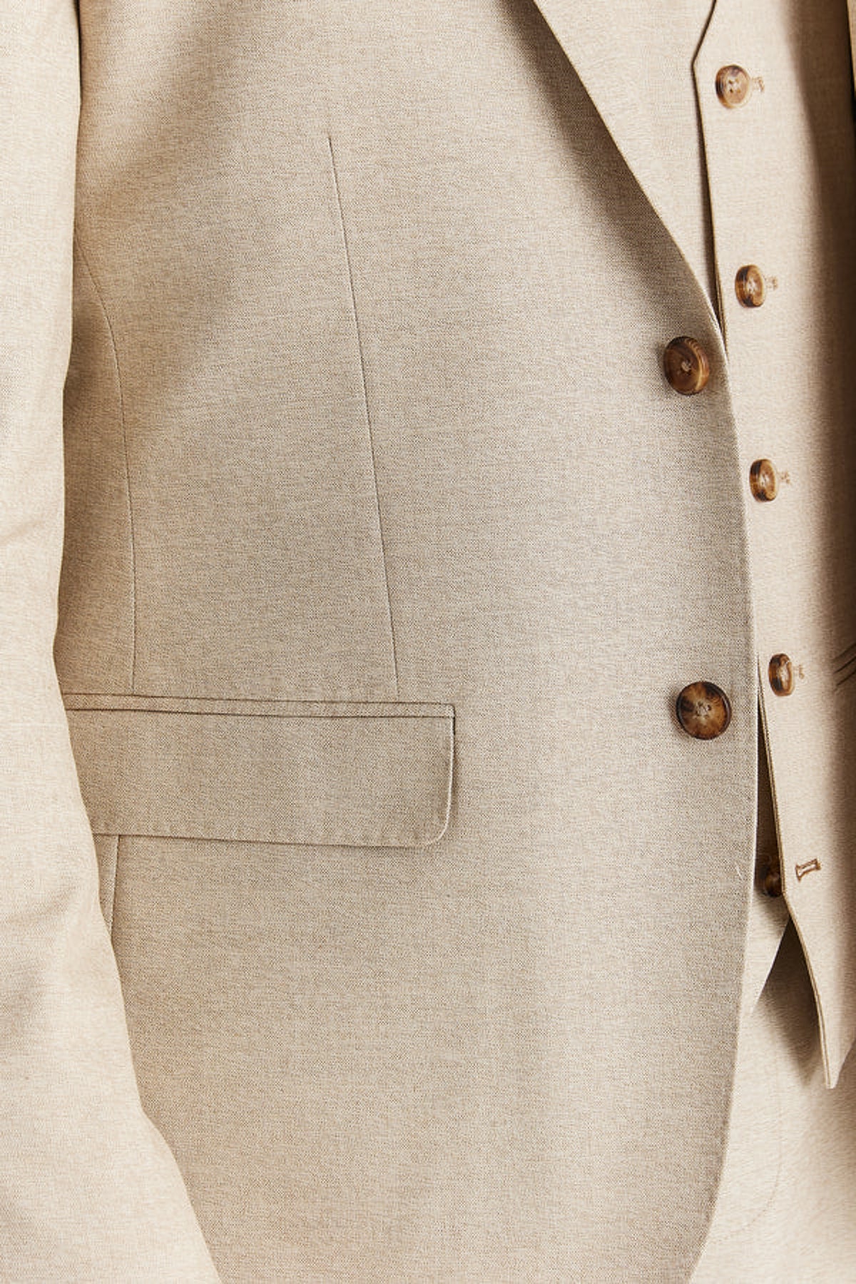 Close-up of a light beige suit jacket with a matching vest underneath, featuring brown buttons and a textured fabric.