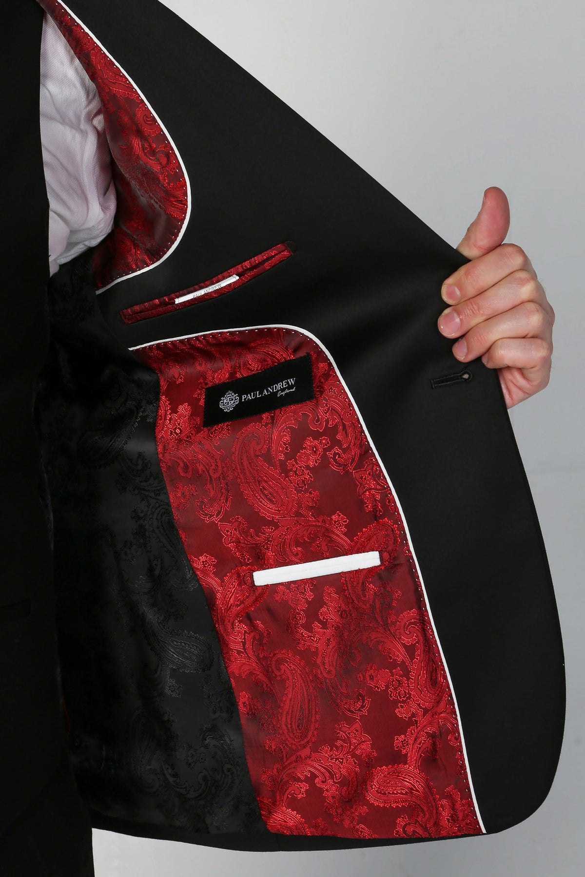 Close-up of a black suit jacket being opened to show a red paisley patterned lining with white piping and a white pocket flap.