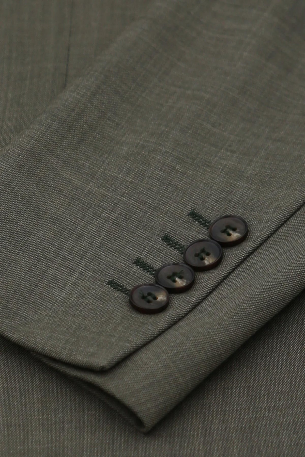Close-up of a folded olive green suit jacket or blazer sleeve showing the fabric texture and a cuff with four dark buttons.