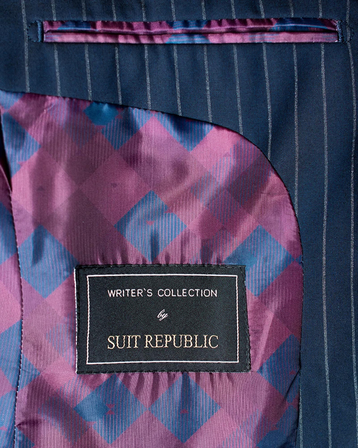 Close-up of a suit jacket's interior lining and pocket. The exterior fabric is navy blue with thin white pinstripes, while the interior lining features a magenta and blue argyle pattern.