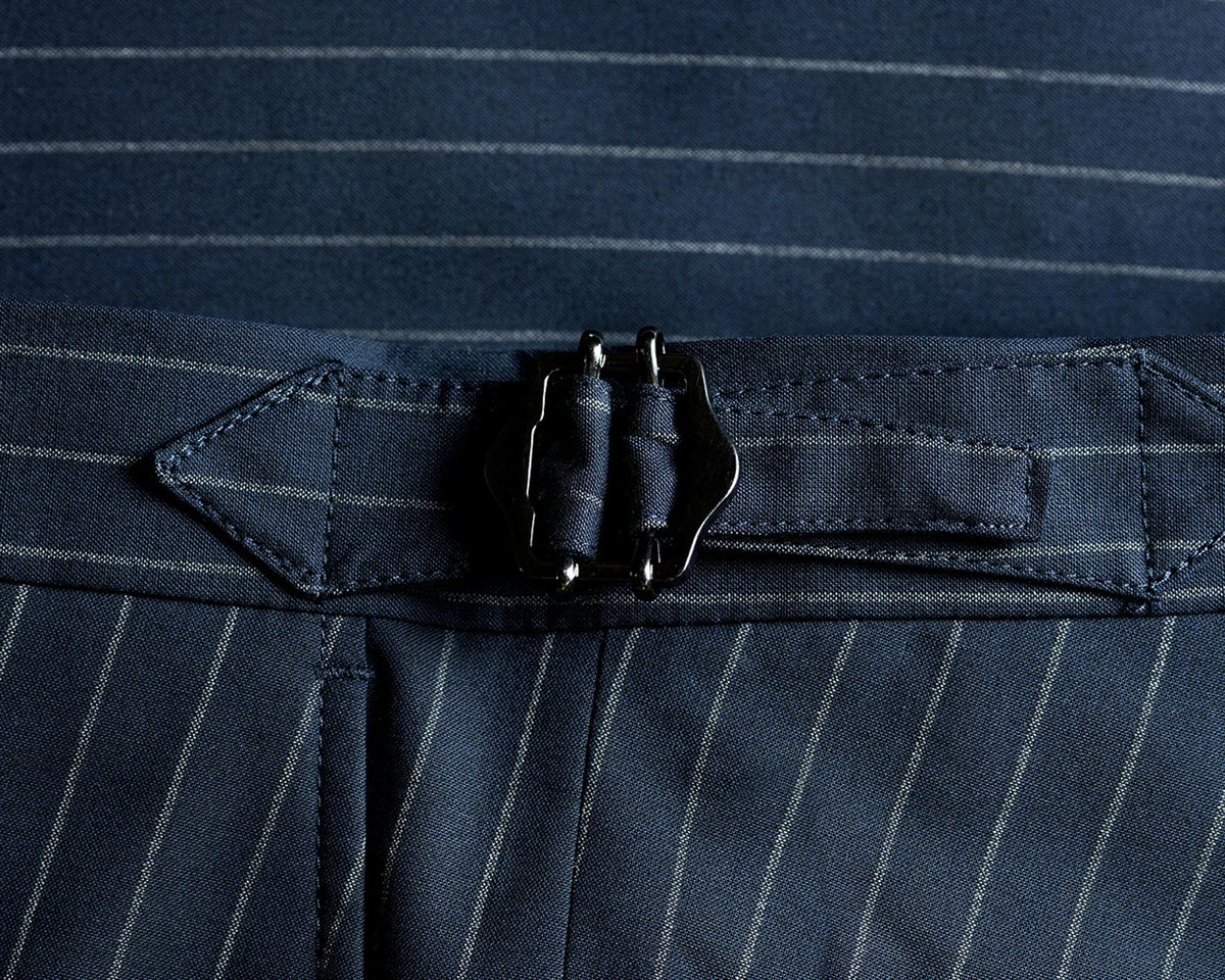 Close-up of navy blue pinstriped trousers with a matching fabric belt and a dark metal buckle.