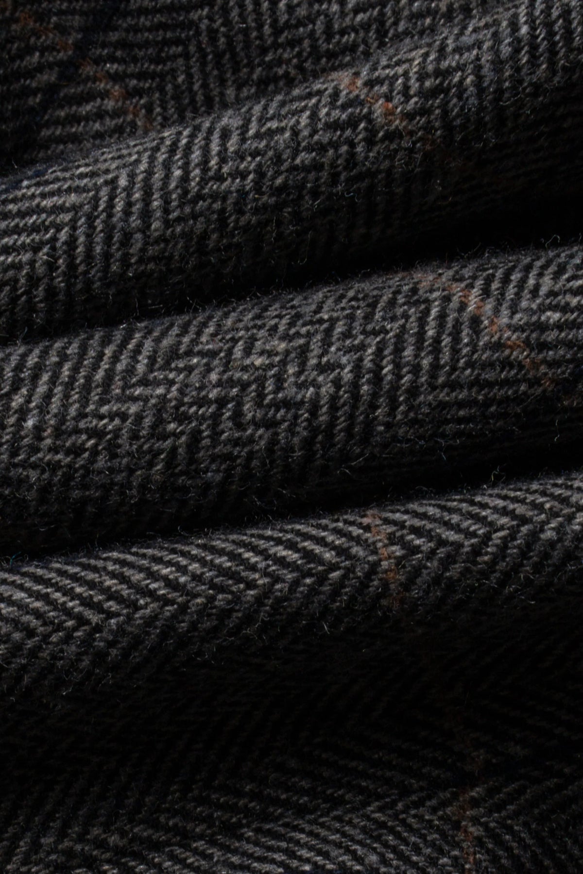 Close-up of a dark charcoal gray herringbone tweed fabric with subtle brown and beige diagonal plaid lines.